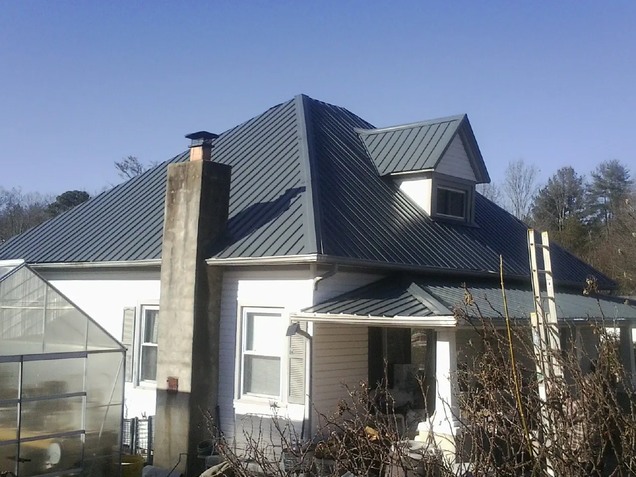 Dark blue standing seam metal roof on a white farmhouse with dormer — Slate & Tile Roof Repair by Roofing Brothers in Brayton