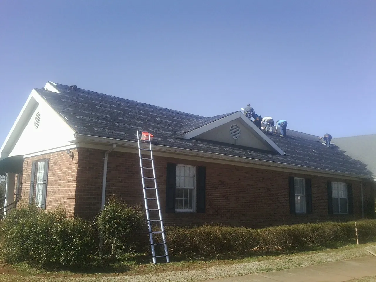 Crew tearing shingles off a brick ranch roof with a ladder set — Emergency Roof Repair work by our crew in Brayton