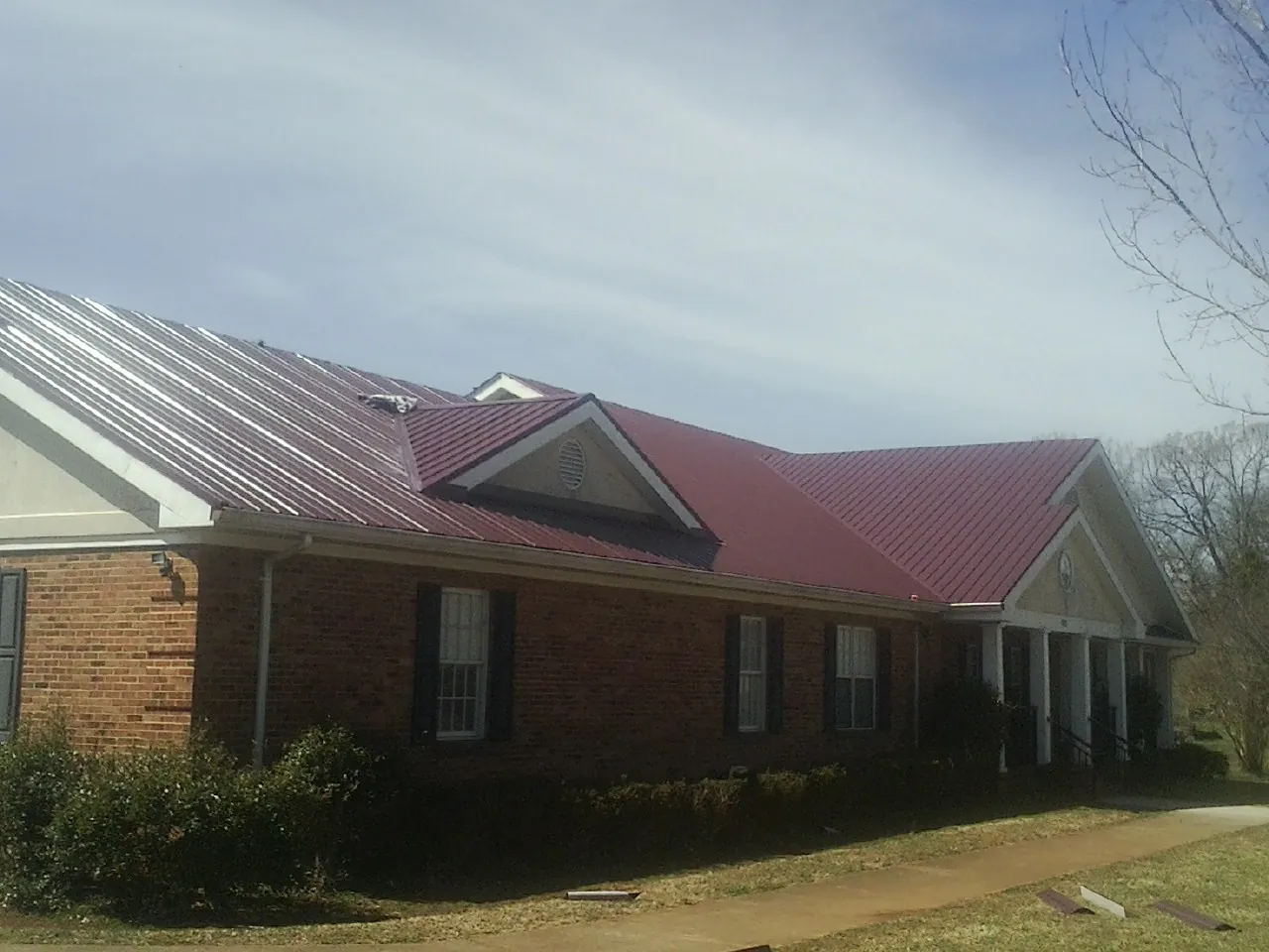 Red metal roof with gabled entries on a long brick building, from a Hail Damage Roof Repair job in Brayton