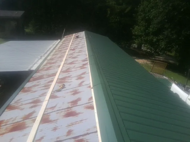 Old rusted panels beside newly installed green metal roofing — Wind Damage Roof Repair by Roofing Brothers in Brayton