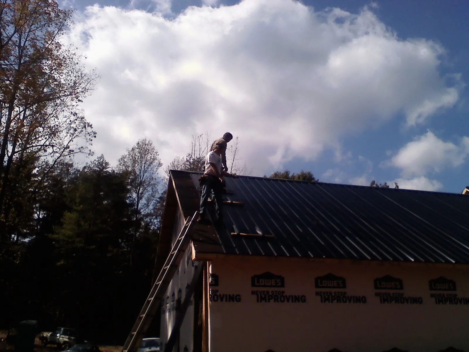 Roofer fastening dark metal panels high against a cloudy sky, from a Roof Inspection job in Brayton