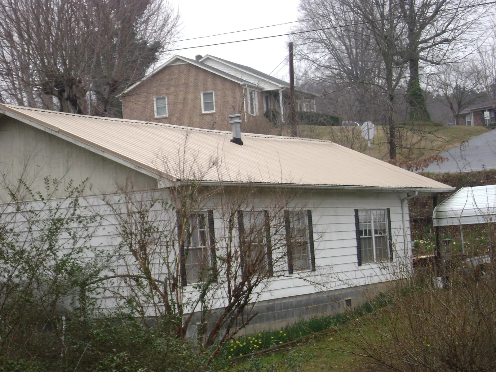 Tan metal roof on a white sided house set into a hillside — Commercial Roofing by Roofing Brothers in Brayton