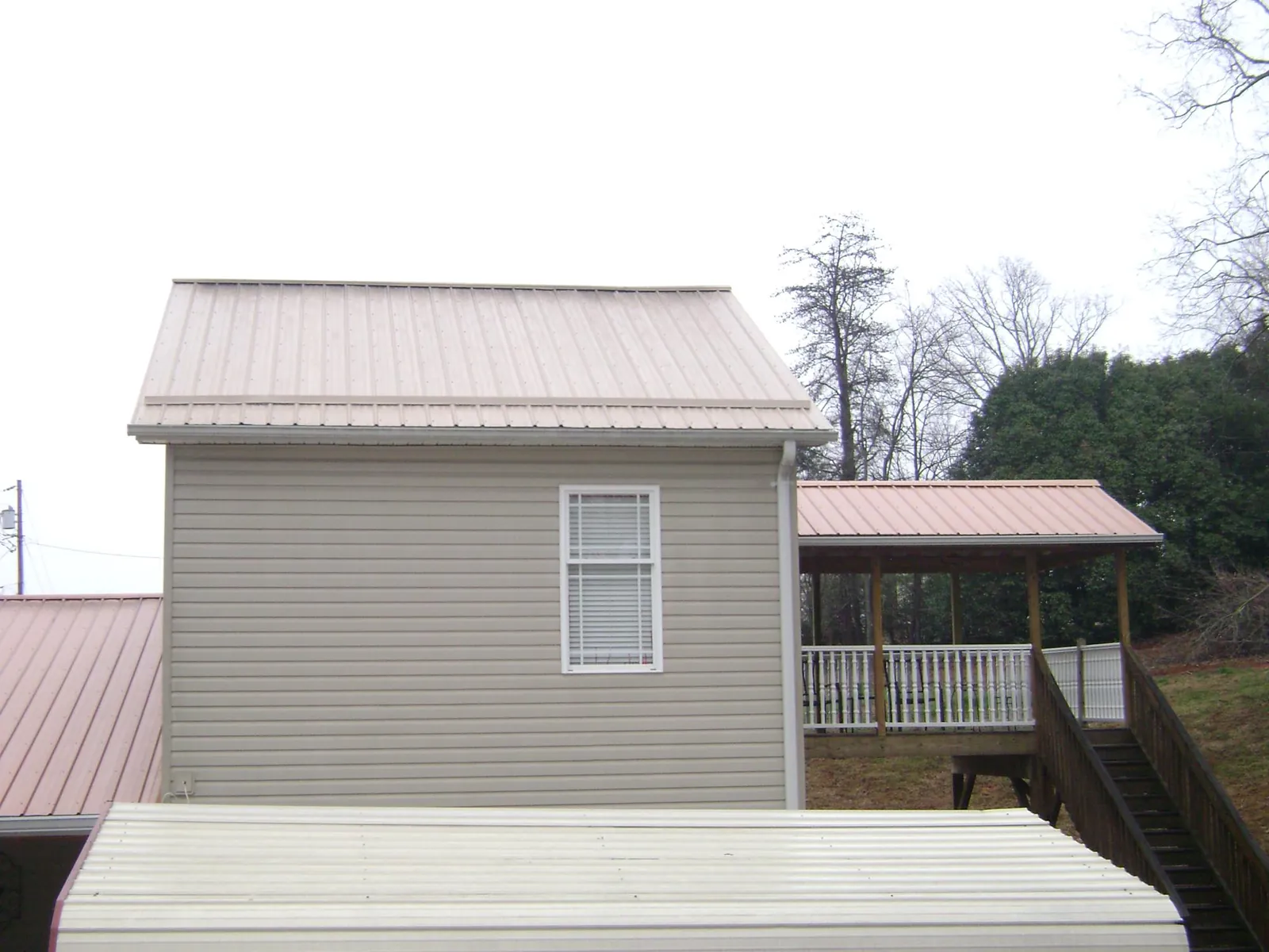 Tan metal roofs on a two story addition and attached porch, from a Roof Replacement job in Brayton